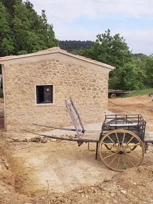 a stone building with a cart in front of it at Bastide Bellugue Maison d'hôtes réseau Bienvenue à La Ferme à 3 minutes de Lourmarin in Cadenet