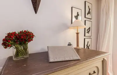 a table with a lamp and a vase of red flowers at La Louvière des Bruyères in Robion en Luberon