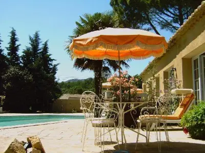 a table with an umbrella and chairs next to a pool at Gites Climatisés Piscine Chauffée La Balancelle in Saint-Rémy-de-Provence