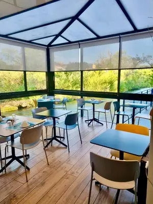 a cafeteria with tables and chairs and windows at Hotel Cantosorgue in LʼIsle-sur-la-Sorgue