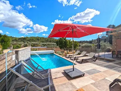 a swimming pool with a red umbrella and chairs at Le Panorama des Alpilles in Aureille