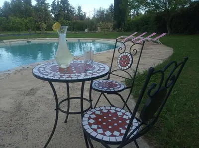 a table and chairs with a vase on it next to a pool at le Mas de la Jardine in Velleron