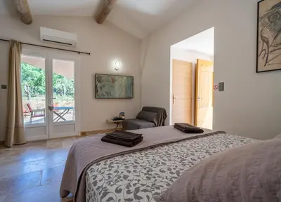 a bedroom with a bed and a chair and a window at Mas la Chêneraie Lourmarin - Au calme, à 10 mn du centre ville à pied in Lourmarin