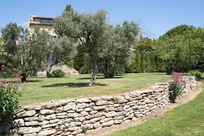 a stone wall in a garden with trees and flowers at Domaine de l'Enclos in Gordes