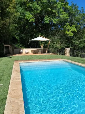 a blue swimming pool in a yard with an umbrella at Le Vieux Moulin de Jouques in Jouques
