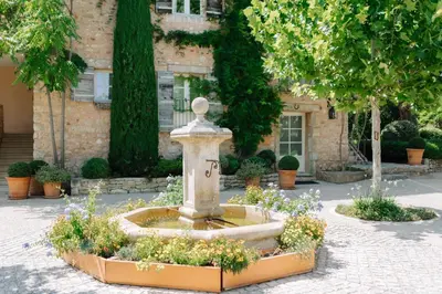 a fountain in a courtyard with flowers in front of a building at Coquillade Provence - Relais & Châteaux in Gargas