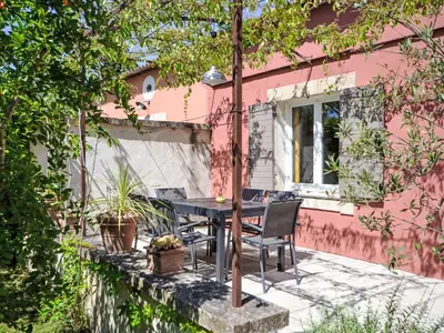 a patio with a table and chairs in front of a pink house at Holiday Home L'Olivier by Interhome in Lagnes