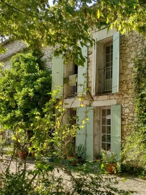 an old stone building with green shutters and a window at Le Mas d'Hermès in Plan-dʼOrgon