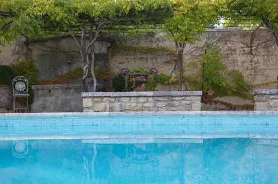 a blue swimming pool with a man sitting next to it at gîte Mas Antinea in Mazan