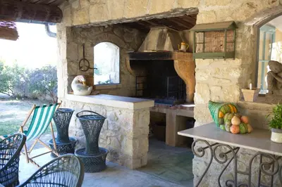 an outdoor kitchen with a stone stove and chairs at gîte Mas Antinea in Mazan