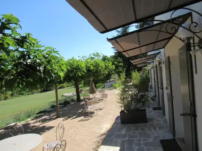 a patio with chairs and tables and a umbrella at Résidence de gîtes La Sidoine du Mont-Ventoux in Crillon-le-Brave