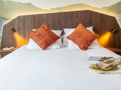 a bed with orange and white pillows on it at Mercure Aix-en-Provence La Duranne Gare TGV in Aix-en-Provence