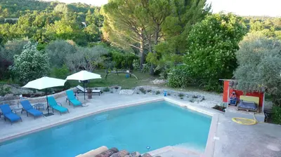 a swimming pool with blue chairs and umbrellas next to at Le mas de la diligence in Mirabeau