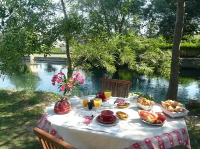 a table with food on it next to a river at Mas Le Pont des Aubes in LʼIsle-sur-la-Sorgue