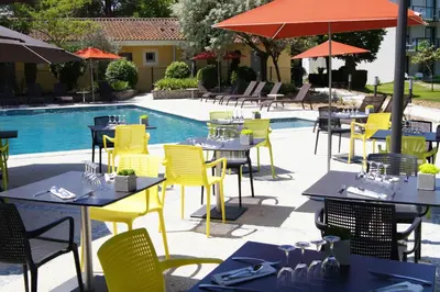 a restaurant with yellow tables and chairs next to a pool at SOWELL HOTELS Domaine de la Petite Isle in LʼIsle-sur-la-Sorgue