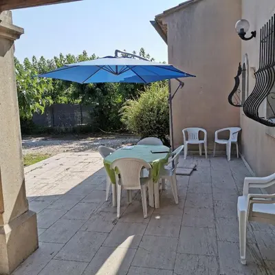 a patio with a table and chairs and a blue umbrella at Aux portes du Luberon in Cheval-Blanc