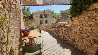 a patio with a wooden table and a stone wall at Sous le Château in Rustrel