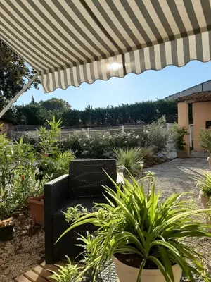 a patio with a black chair under a striped umbrella at le Mas d'Hubert in LʼIsle-sur-la-Sorgue