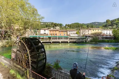 a man is fishing on a river with a bridge at Charmante maison de village à Fontaine-de-Vaucluse in Fontaine-de-Vaucluse