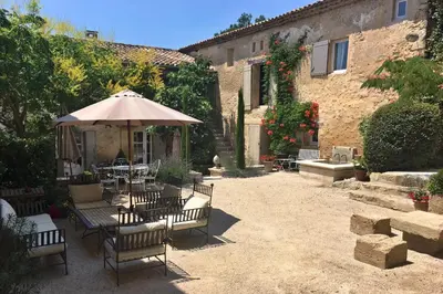 an outdoor patio with an umbrella and tables and chairs at Château de la Merletade in Cheval-Blanc