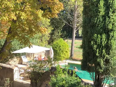 a pool with an umbrella and two people in it at Le Mas de la Sorgue in Le Thor