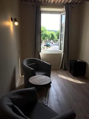 a living room with a chair and a table and a window at Le Cheval Blanc in La Bastide-des-Jourdans