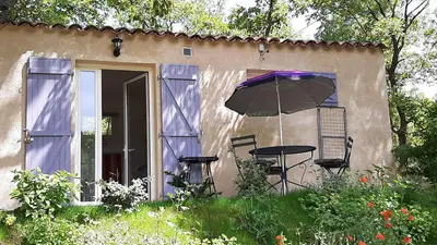 a table and chairs and an umbrella in front of a house at Le Cabanon in Sainte-Croix-à-Lauze
