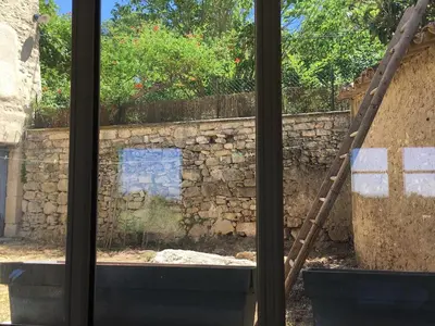 a window view of a stone wall and a ladder at l'Ecurie in Bonnieux