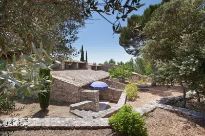 a garden with a stone house with a blue umbrella at Résidence Odalys La Bastide des Chênes in Gordes