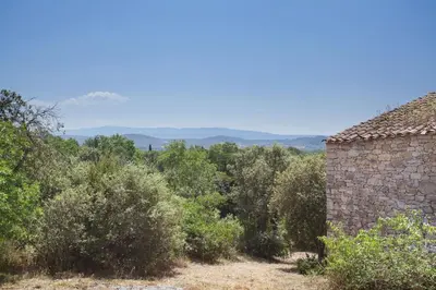 a stone building in a field of trees and bushes at Résidence Odalys La Bastide des Chênes in Gordes