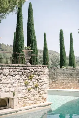 a stone wall and a swimming pool with trees at La Bastide de Marie, Maisons et Hôtels Sibuet in Ménerbes