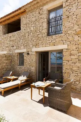 a patio with chairs and tables in front of a stone building at Mas des Herbes Blanches Hôtel & Spa – Relais & Châteaux in Joucas