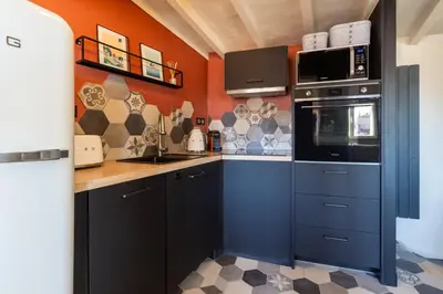 a kitchen with black cabinets and an orange wall at DUPLEX MIRABEAU - Roof terrace with panoramic view in Aix-en-Provence