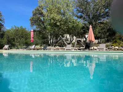 a large pool of blue water with chairs and an umbrella at Lou Mas in Gordes