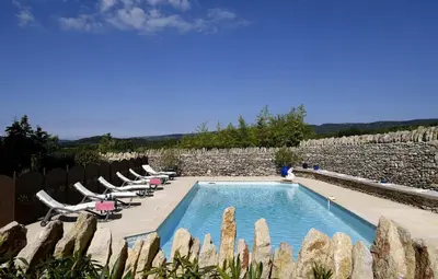 a swimming pool with lounge chairs and a stone wall at Bastide Des Demoiselles in Roussillon