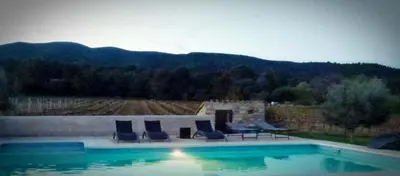 a swimming pool with chairs and a table and mountains at Appartement St Victor in Puyvert