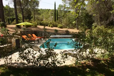 a swimming pool in a yard with chairs and an umbrella at Logis au milieu des pins in Le Puy-Sainte-Réparade
