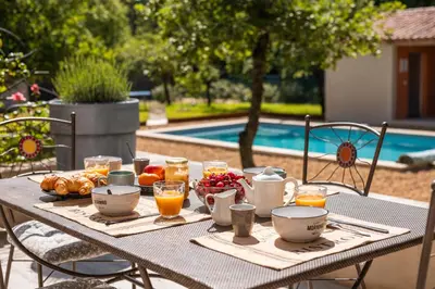 a table with breakfast foods and drinks on it next to a pool at Le JARDIN DES DELIS gite NEUF avec piscine bio UV in Saint-Saturnin-les-Apt