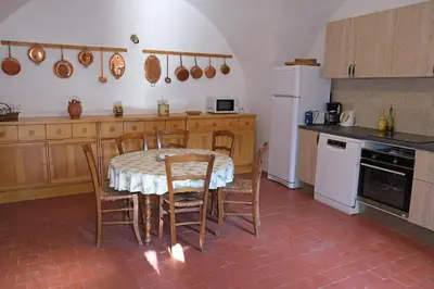 a kitchen with a table and chairs and a white refrigerator at typical mas provençal with swimming pool in a small hamlet near mouriès in the alpilles in provence- 8 persons in Mouriès