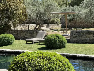 a garden with a bench and a umbrella and a pond at Le Mas de Béthel in Gordes
