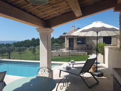 a patio with an umbrella and chairs and a pool at Bastide Toujours Dimanche, Maison de vacances avec vue & piscine chauffée in Gordes