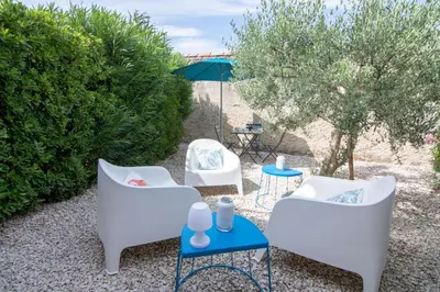 a patio with white chairs and a table with an umbrella at L'Isle Ô Jardin in LʼIsle-sur-la-Sorgue