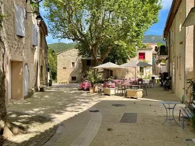 an alley with tables and umbrellas in a village at Maison & Jardin Coeur Luberon classé 4 étoiles in Peypin-dʼAigues