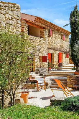 a stone house with a table and chairs in front of it at Villa élégante avec piscine privée à Ansouis, vues montagne in Ansouis