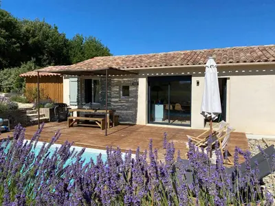 a patio with an umbrella and some purple flowers at Villa pleine campagne, piscine chauffée , Lubéron in Lacoste