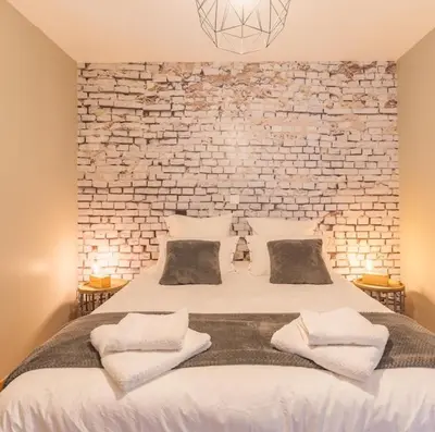 a bedroom with a white bed with a brick wall at Domaine Plan des Devens in Roussillon