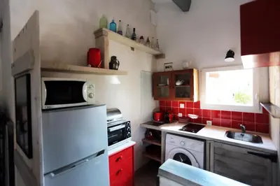 a small kitchen with a white refrigerator and red cabinets at LUBERON DES ARTISTES 2 in Apt