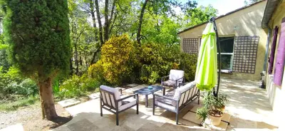 a patio with a table and a green umbrella and chairs at Villa Chênaie in Bédoin