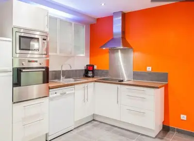 a kitchen with white cabinets and an orange wall at Appartement de Charme in Aix-en-Provence