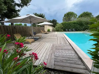 a wooden deck with chairs and an umbrella next to a swimming pool at Mas de l'Estiou in Monteux